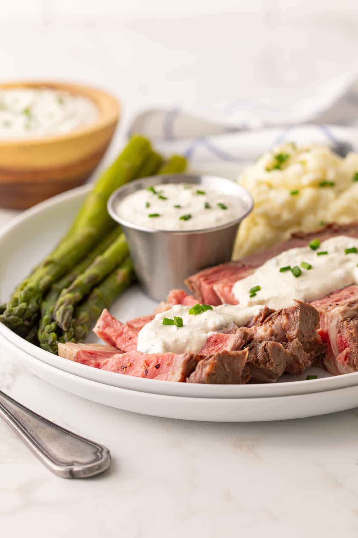 Front view of a sliced prime rib topped with horseradish sauce on a white plate.