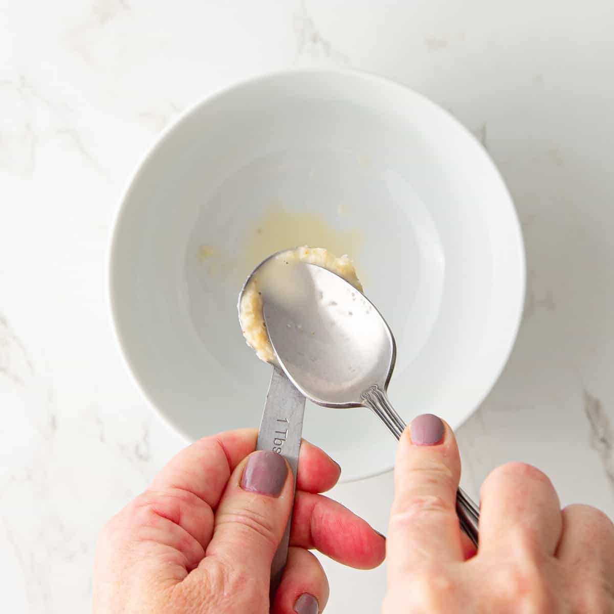 A spoon pressing on a tablespoon of prepared horseradish draining off the liquid.