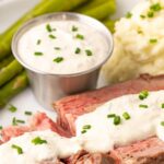 A slice of prime rib on a plate topped with horseradish sauce with overlay text.