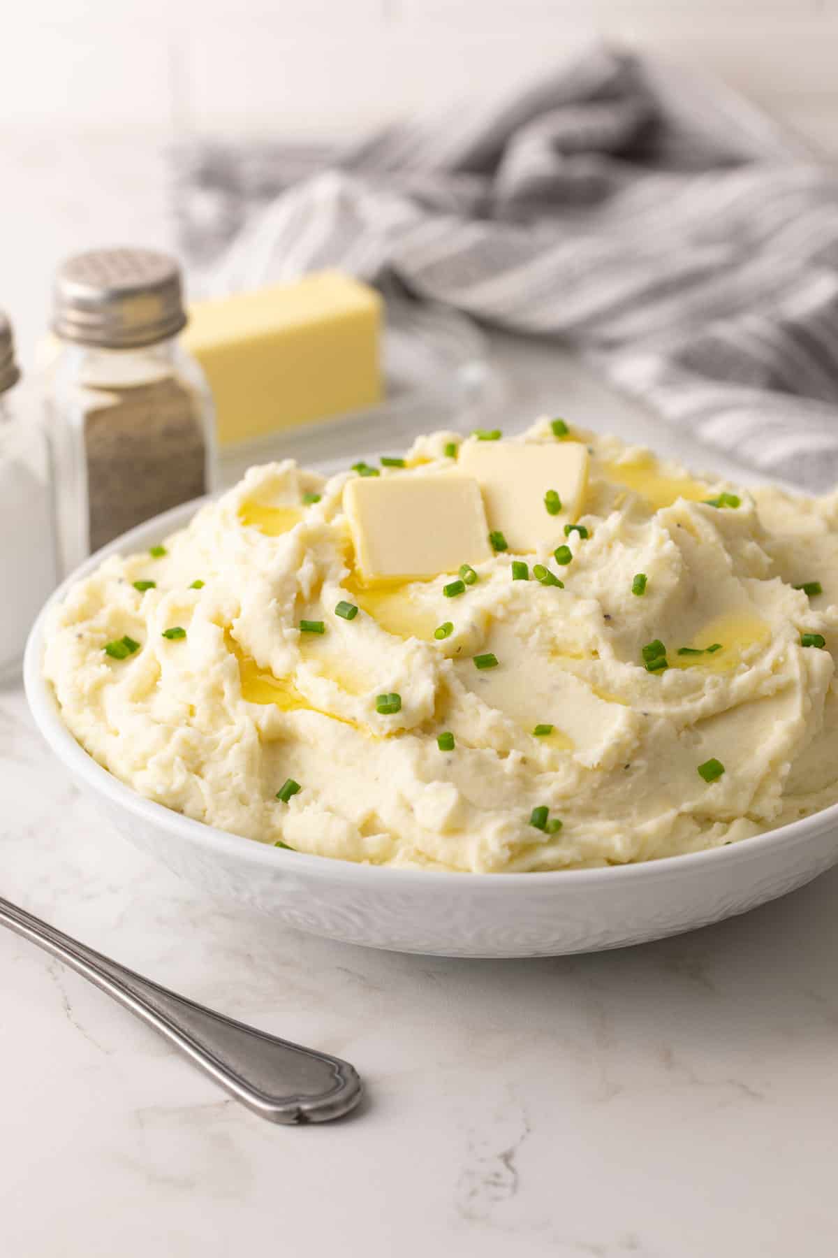 Make-ahead mashed potatoes topped with butter and chives in a white bowl.