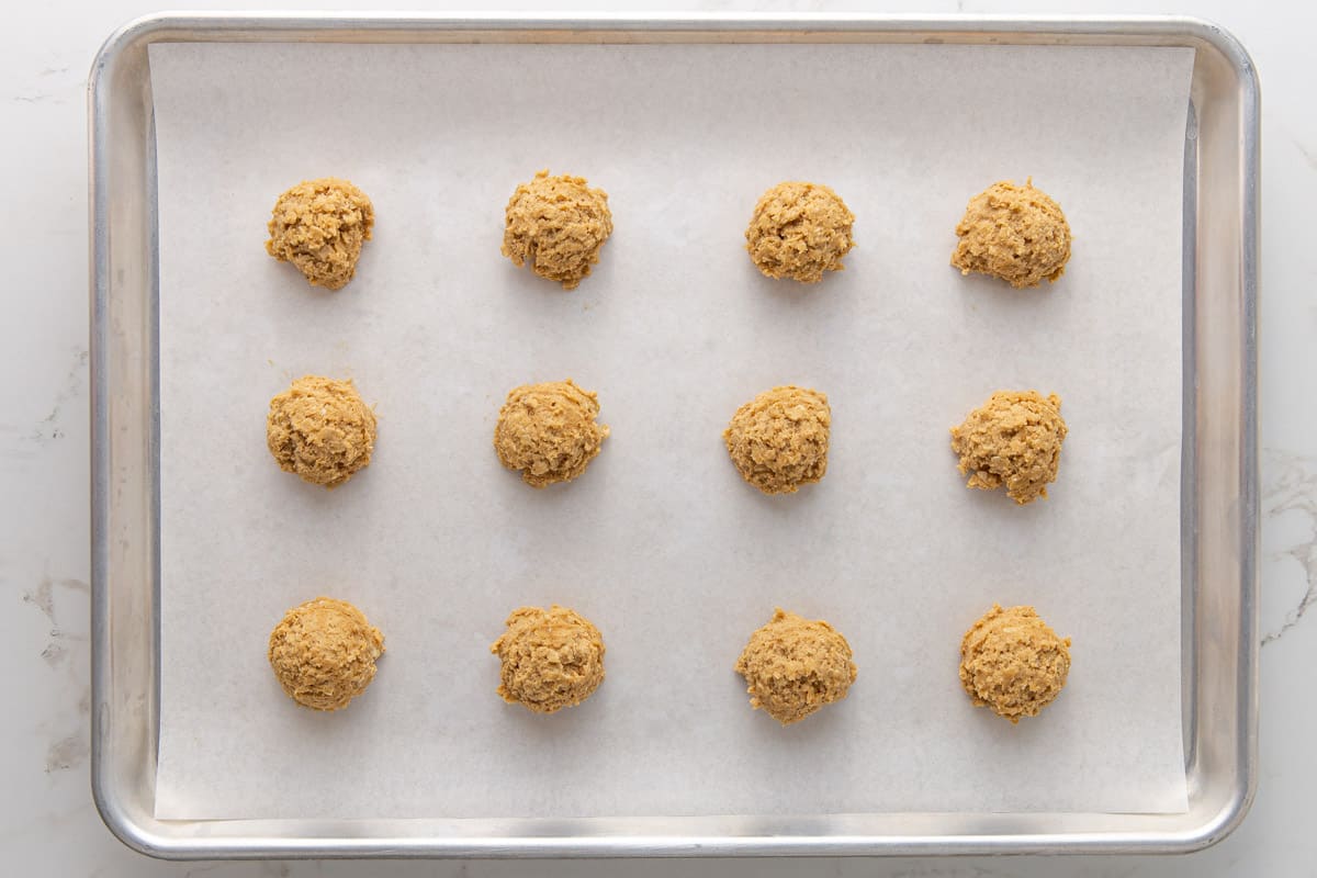 Overhead view of cookie dough balls on a baking sheet that has been lined with parchment paper.
