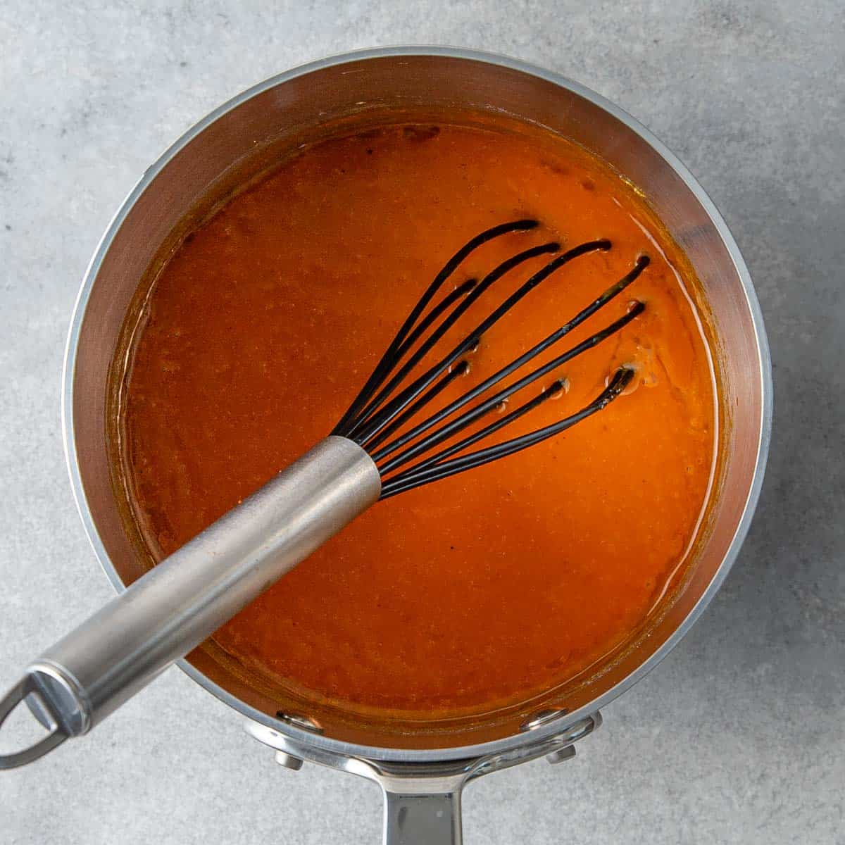 Buffalo wing sauce in a saucepan with a whisk.