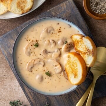 Cream of mushroom soup in a blue bowl with two slices of French bread.
