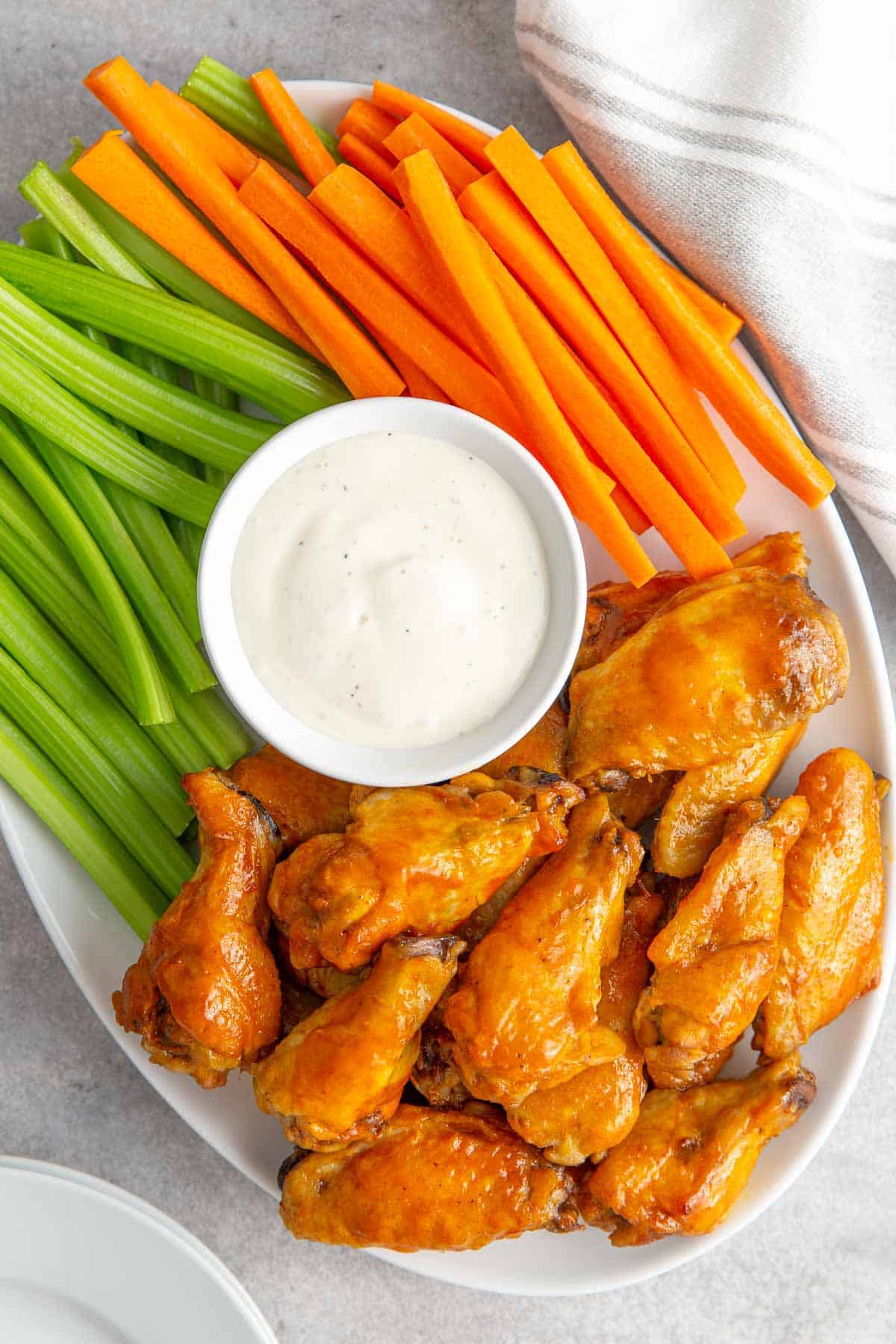 Buffalo wings, celery sticks, carrot sticks and a small bowl of ranch dressing on a white platter.