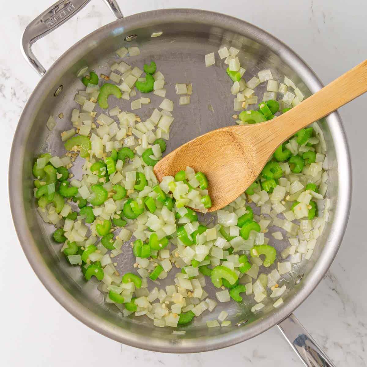 Sautéed celery and onions in a skillet with a wooden spoon.