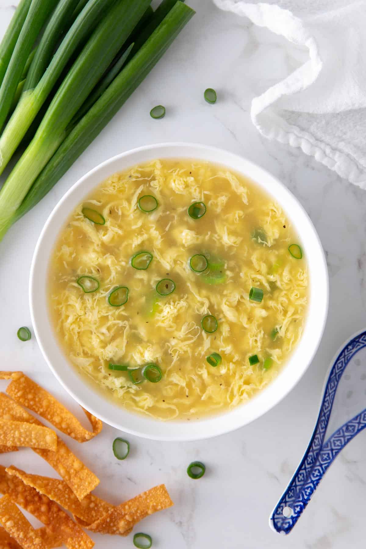 Egg drop soup topped with sliced green onions in a white bowl.  