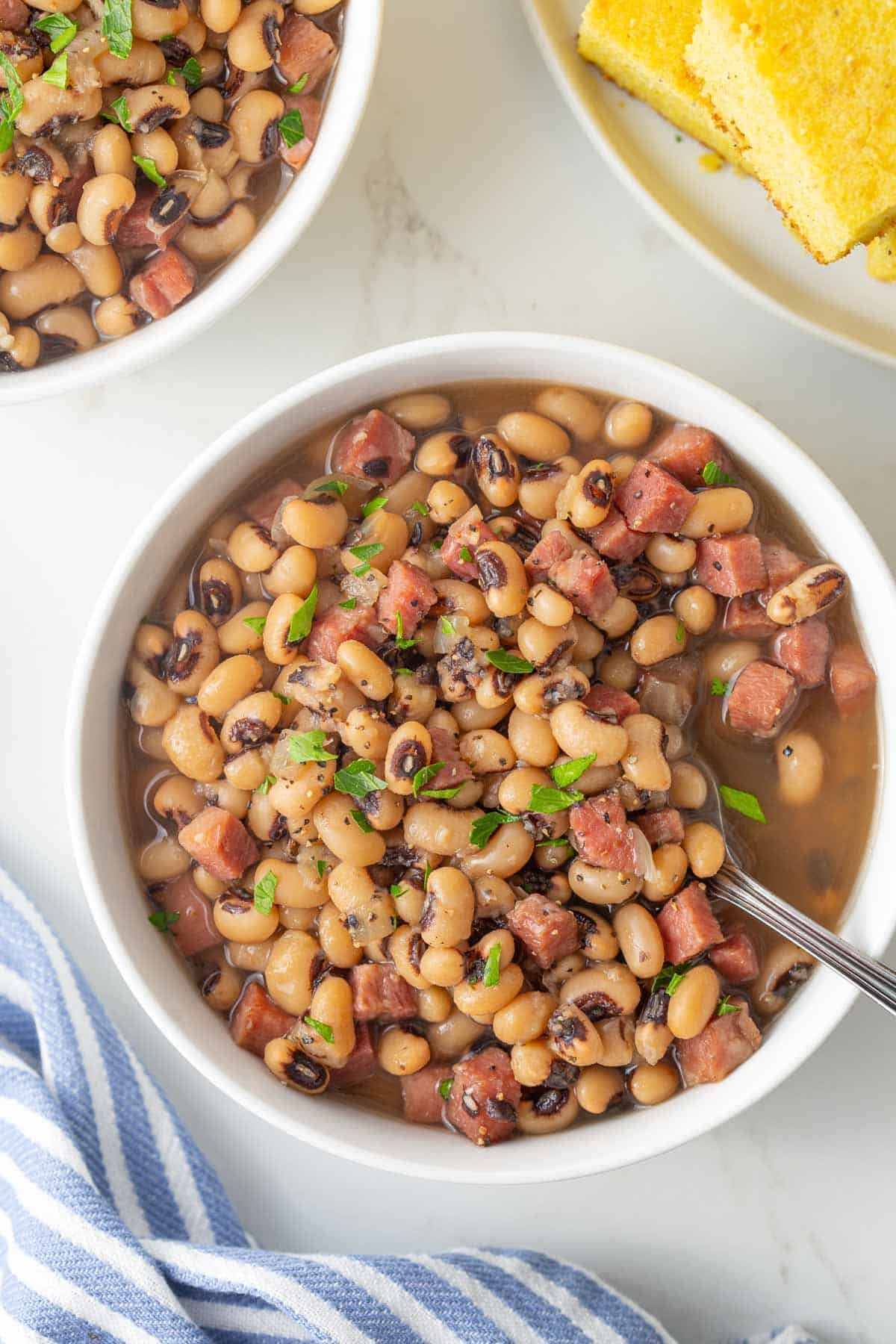 Overhead closeup view of a white bowl of black-eyed peas with a spoon in the bowl.