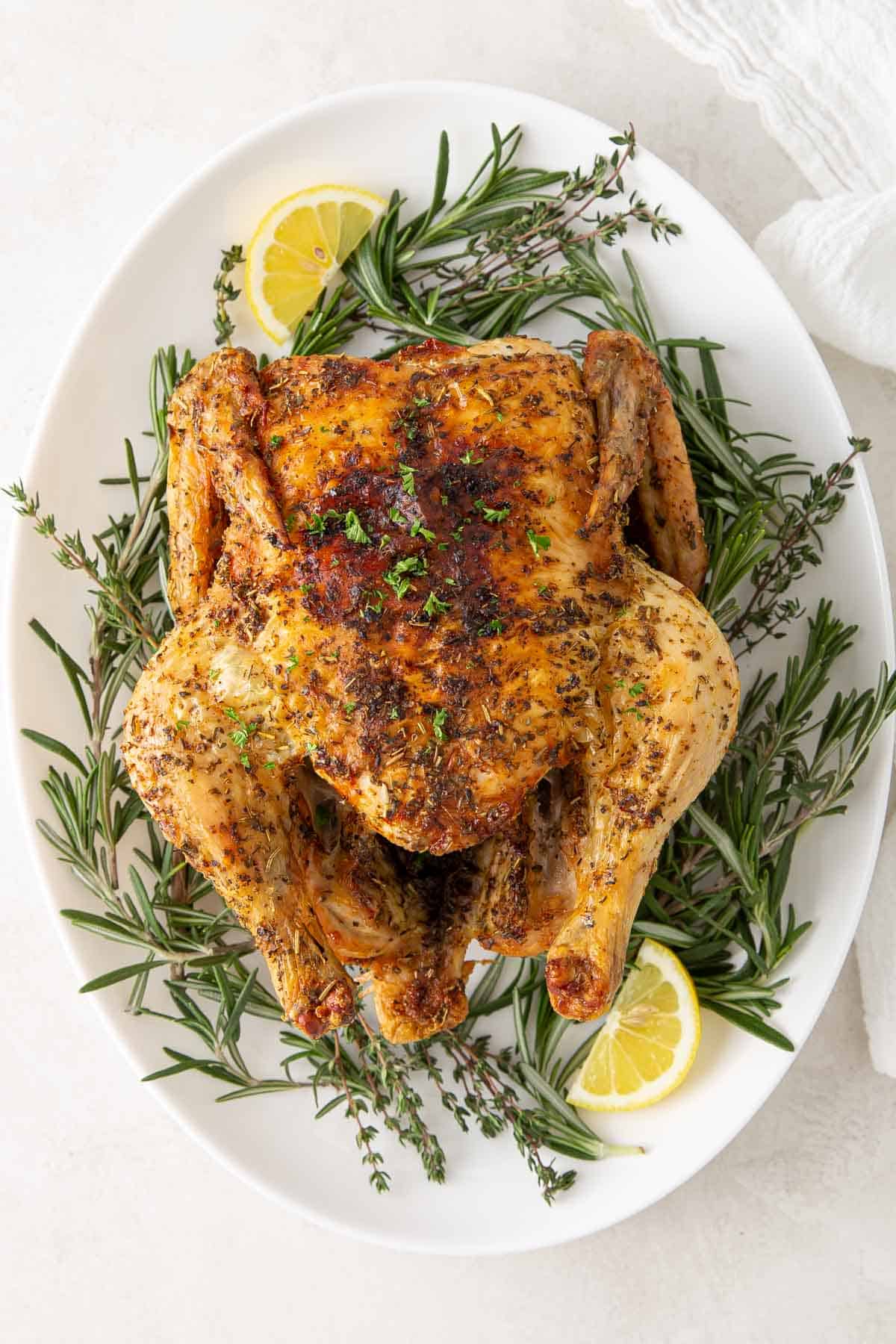 Air fryer chicken on a platter with fresh herbs and lemon wedges.