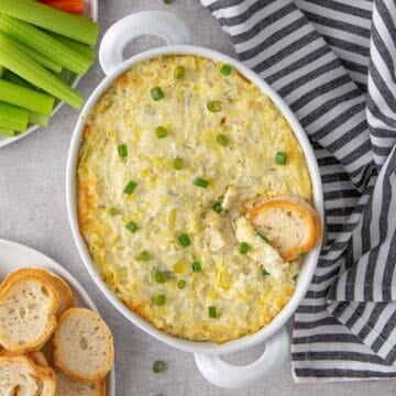 A toasted baguette slice in a white baking dish with baked artichoke dip.