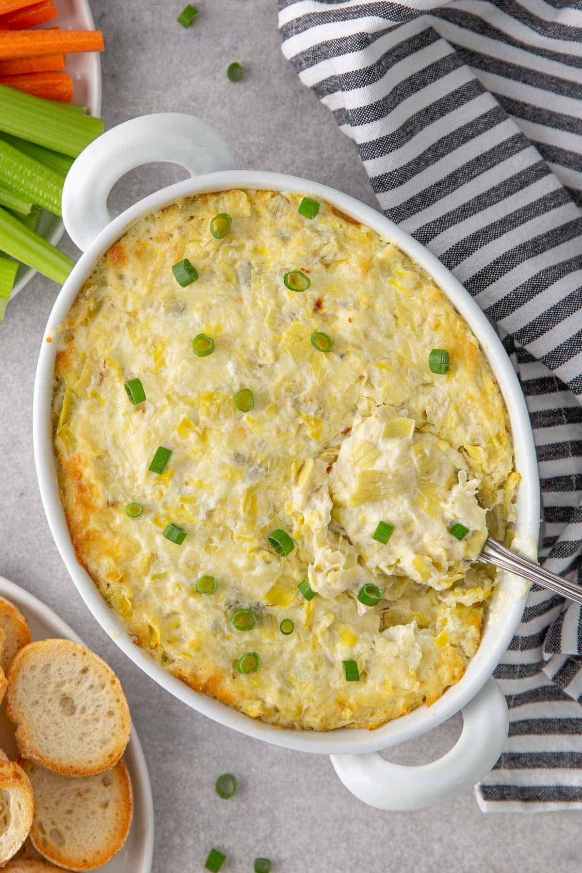 A serving spoon in a dish with baked artichoke dip.