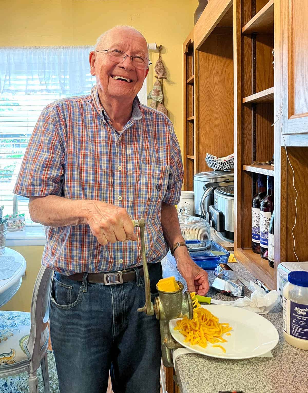 A man using a manual meat grinder to grind cheese for pimento cheese.