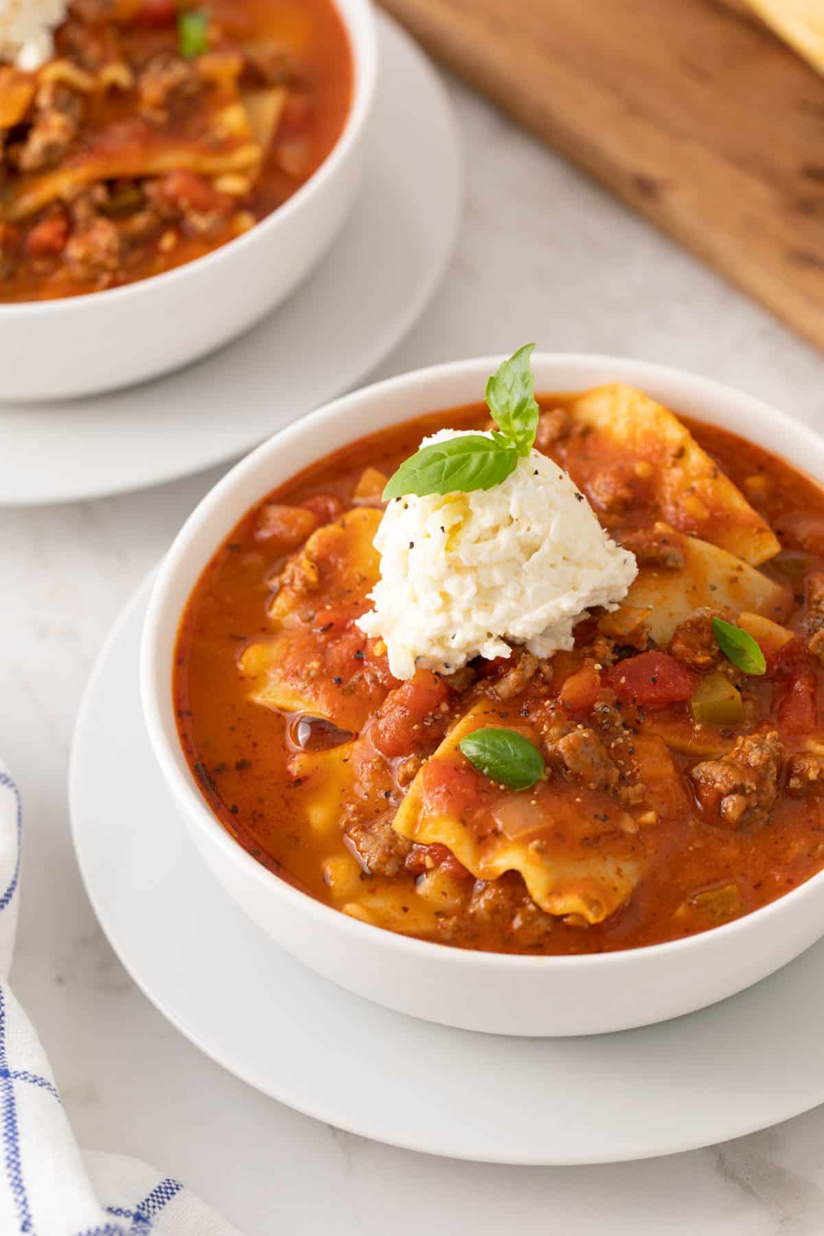 Closeup view of a lasagna soup in a white bowl topped with a dollop of ricotta cheese mixture.