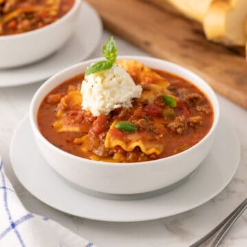 Lasagna soup in a white bowl topped with a dollop of ricotta cheese mixture.
