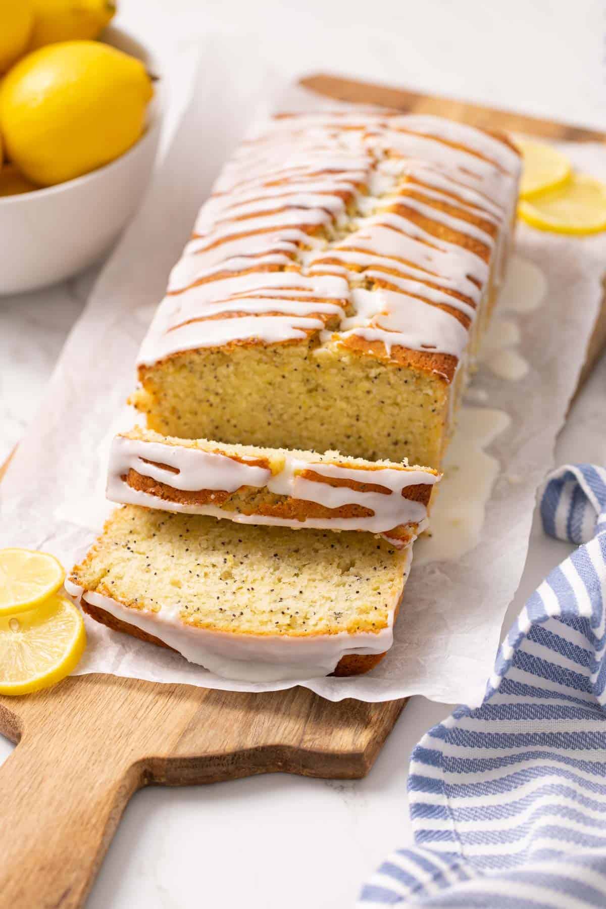 A glazed loaf of lemon poppy seed bread with two slices cut.