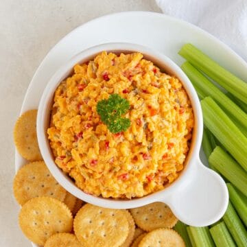 Pimento Cheese Spread in a white bowl topped with a sprig of fresh parsley.
