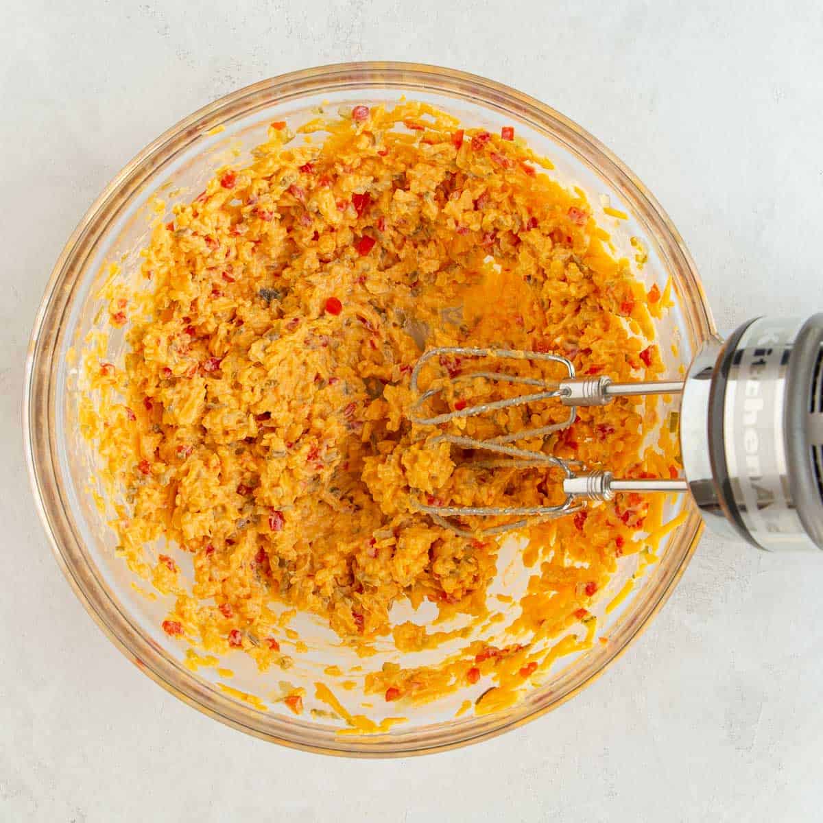 A hand mixer in a mixing bowl with pimento cheese spread.