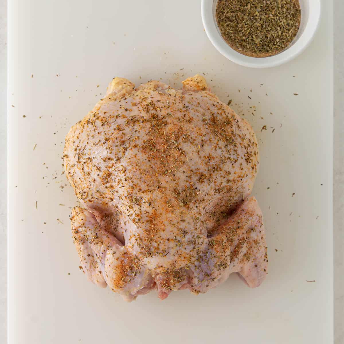 A whole raw chicken that has been coated in olive oil and seasonings before being cooked in an air fryer.