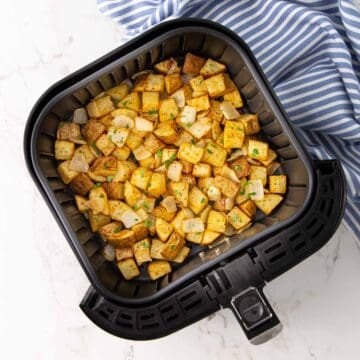 Air-fried potatoes and onions in an air fryer basket.
