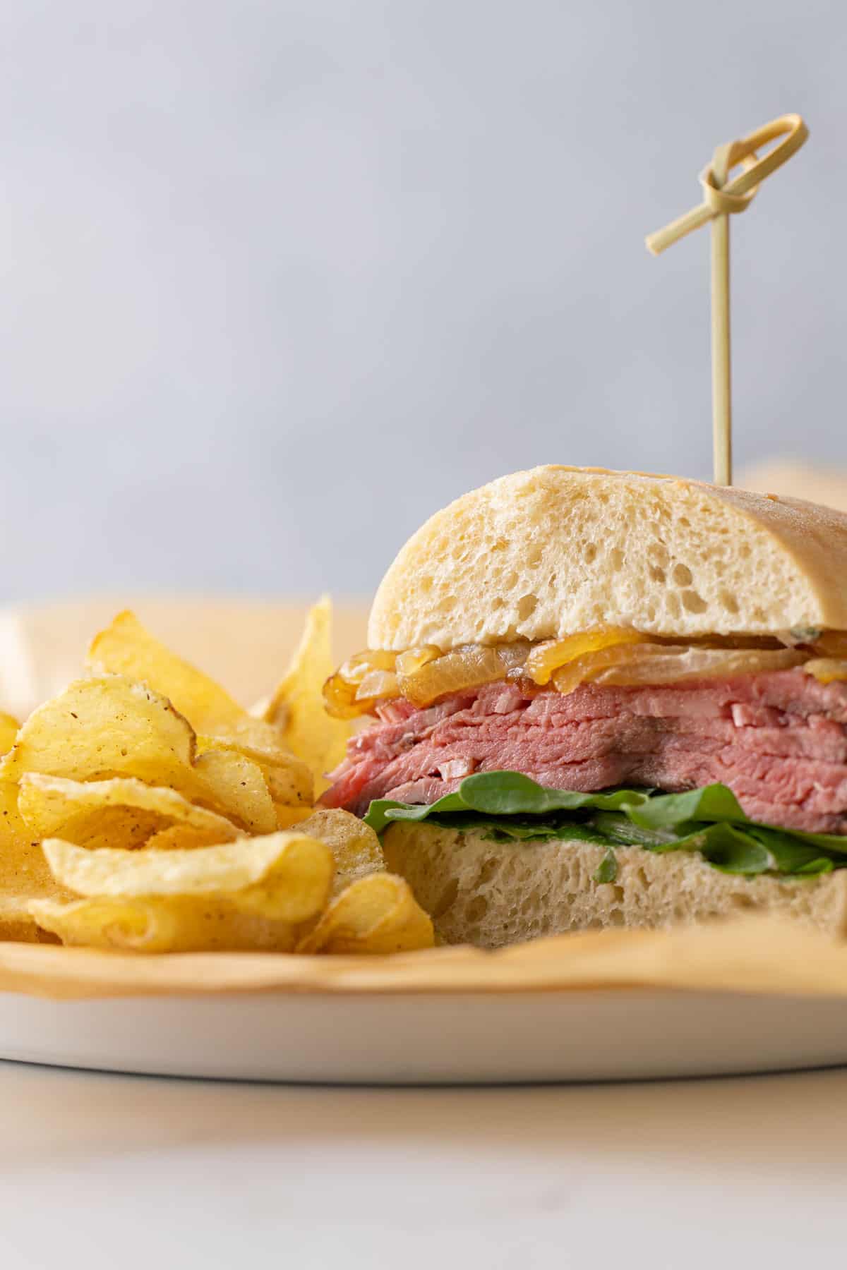 A prime rib sandwich on a plate with potato chips.