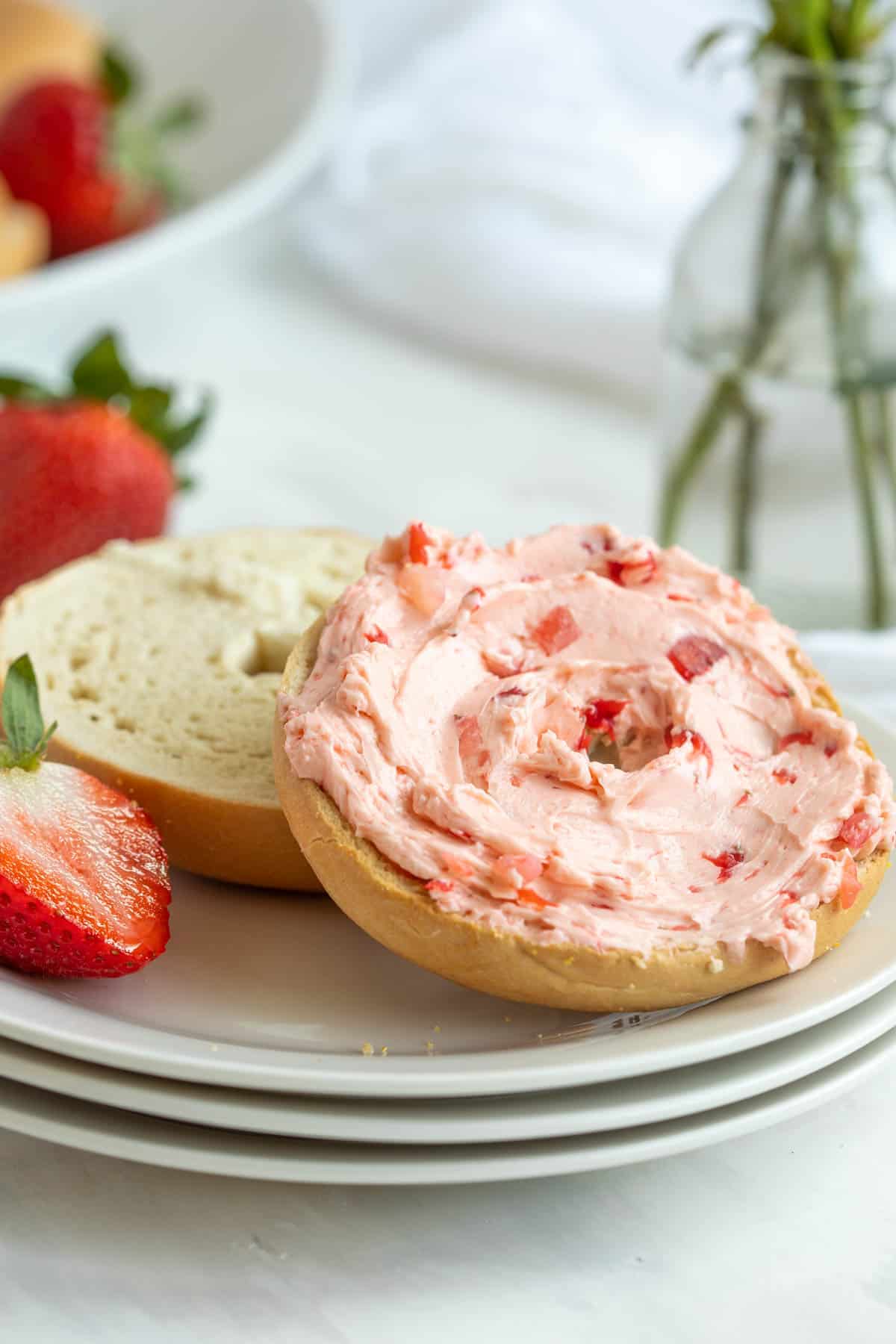 Front view of a bagel that is spread with strawberry honey butter on a white plate.