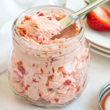 A spreading knife in a jar of strawberry honey butter.