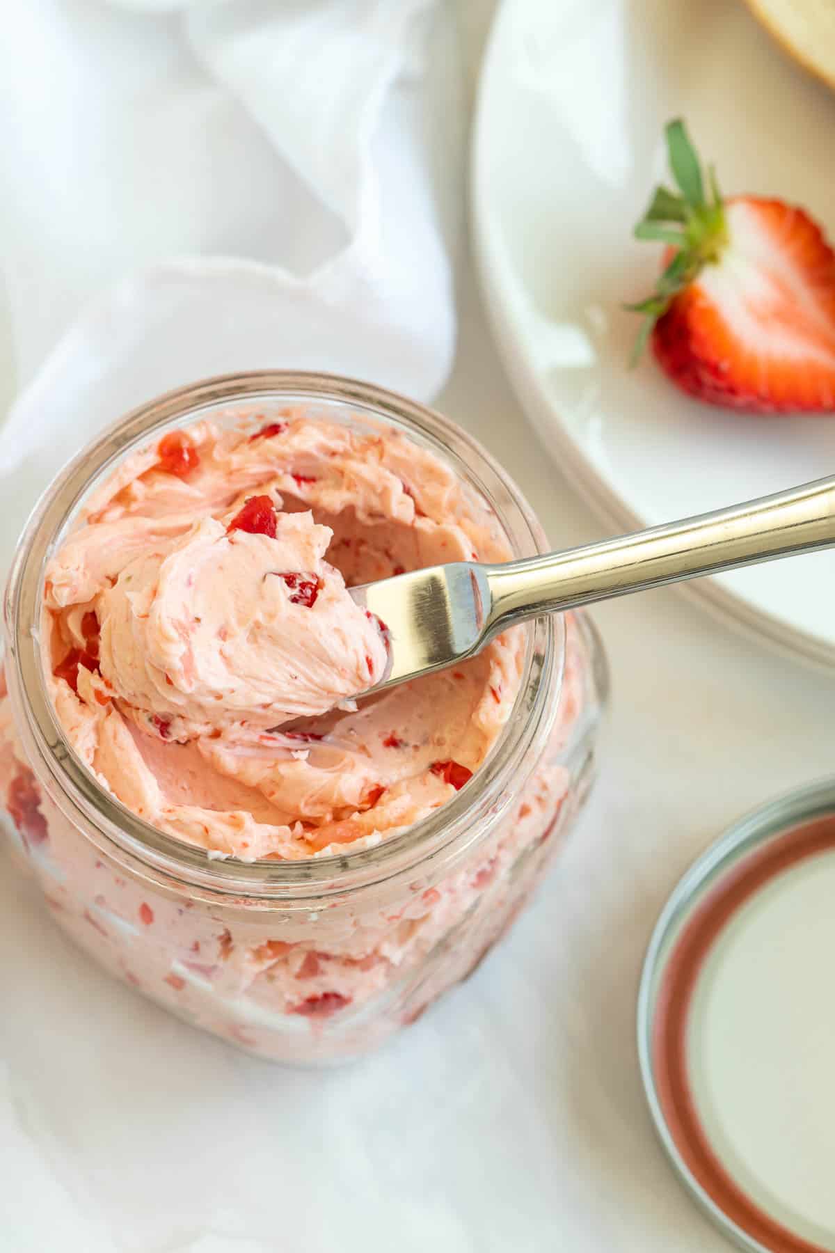 Overhead view of a jar of strawberry honey butter with a spreading butter knife.