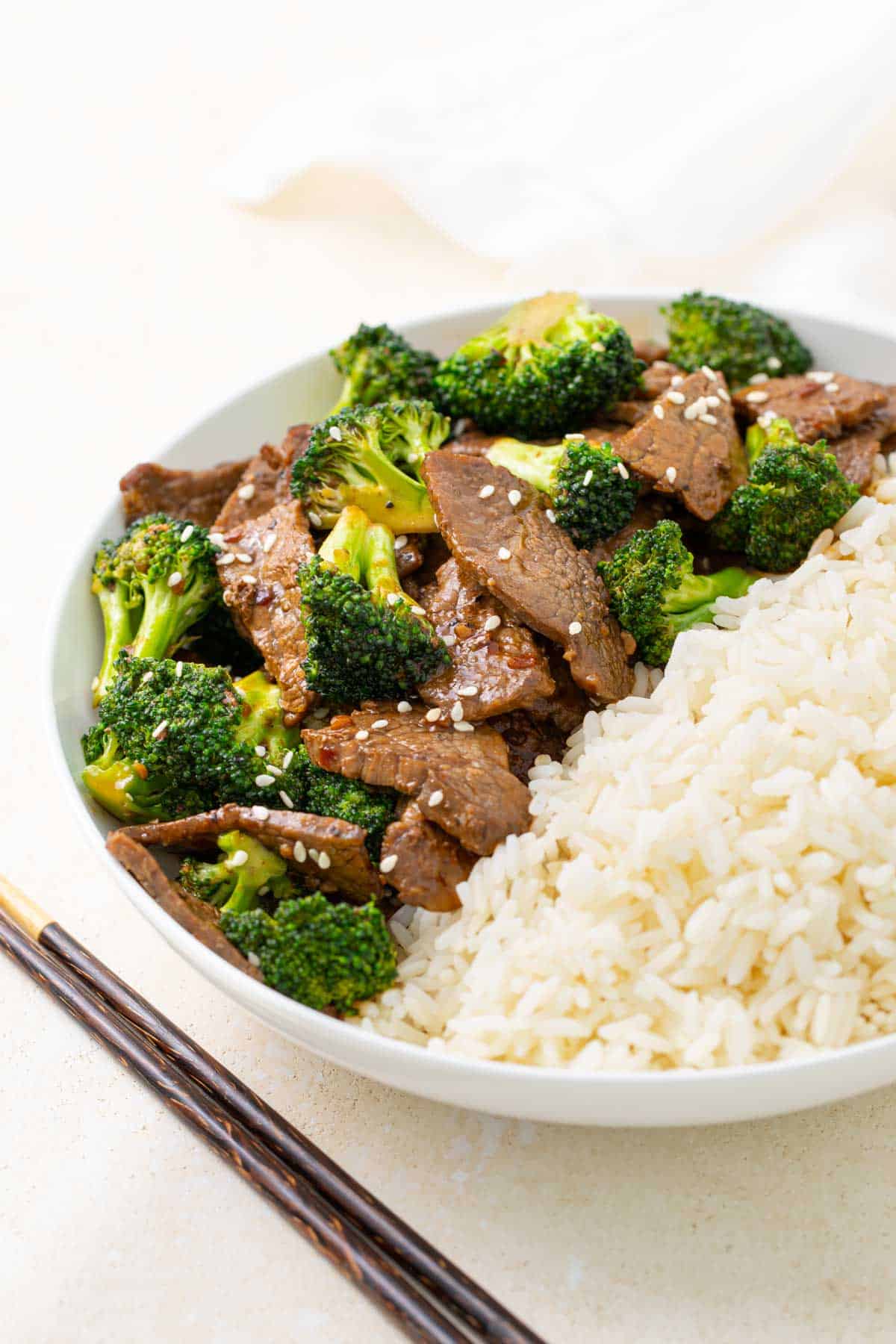 Beef and Broccoli with white rice in a bowl beside a set of chopsticks.