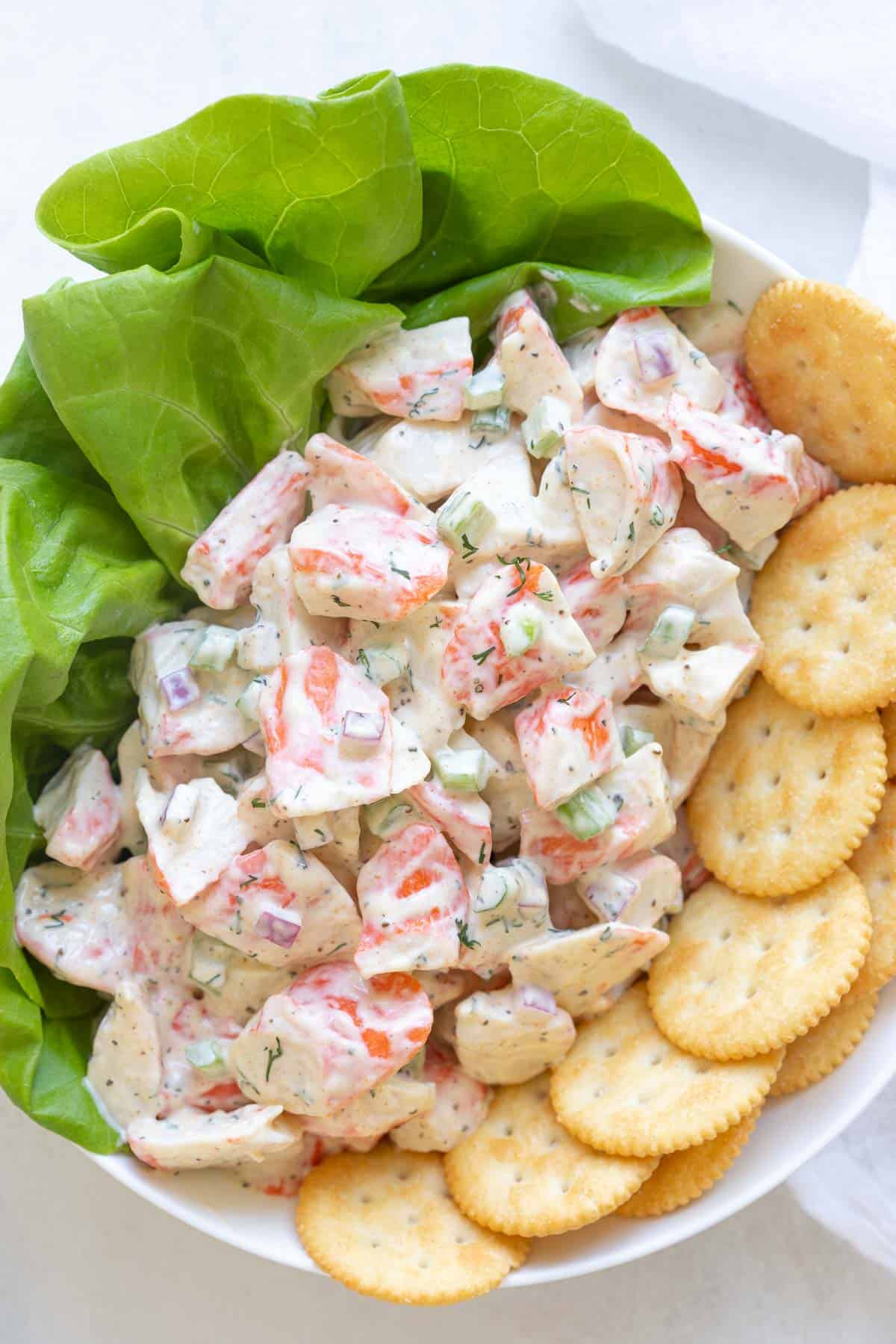 Overhead closeup view of imitation crab salad in a bowl with lettuce and crackers.