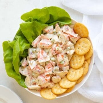 Imitation crab salad in a white bowl with lettuce and round crackers.