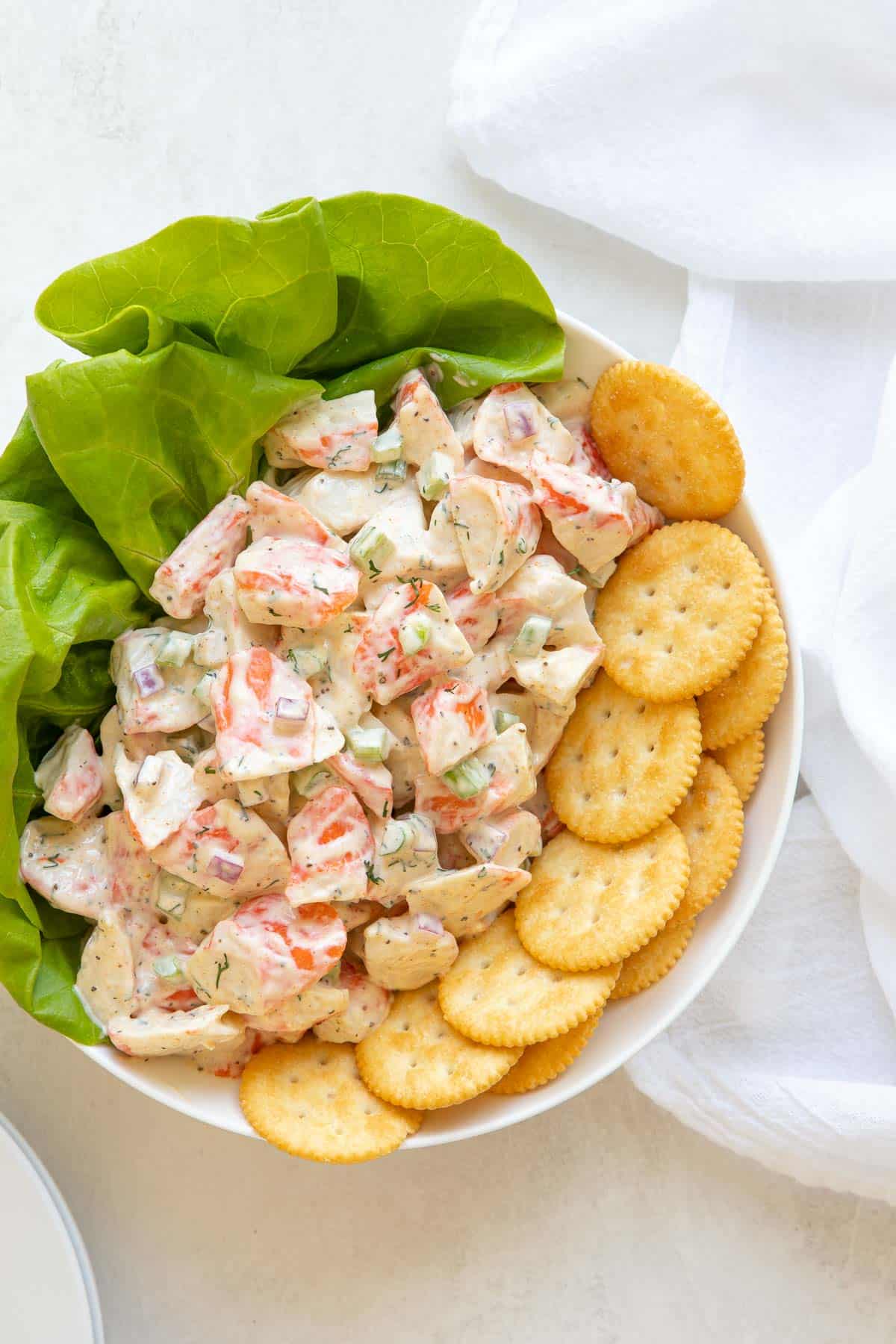 Imitation crab salad in a bowl with lettuce and crackers by a white kitchen towel.