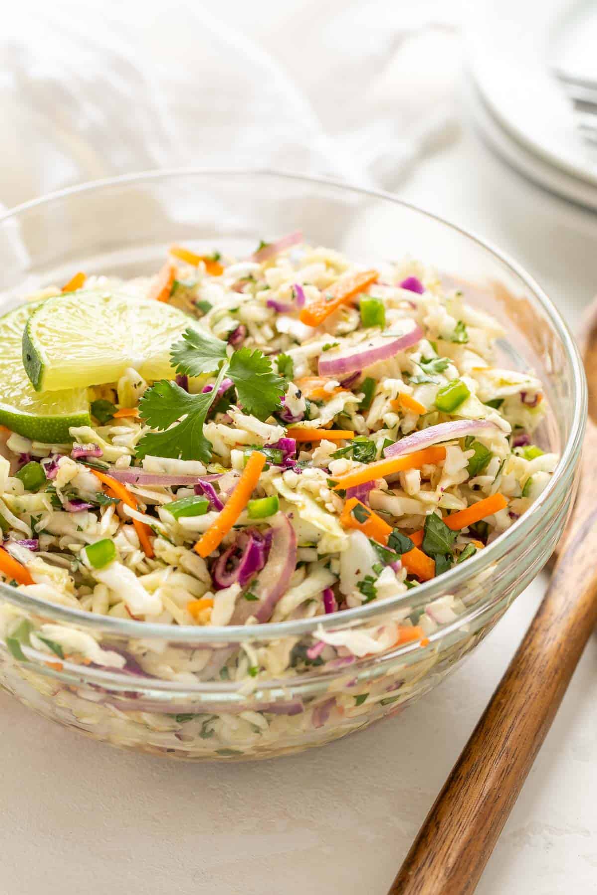 Front angled view of Mexican coleslaw in a bowl beside a set of wooden salad servers.