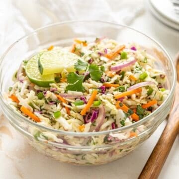 Mexican coleslaw in a bowl beside a set of wooden salad servers.