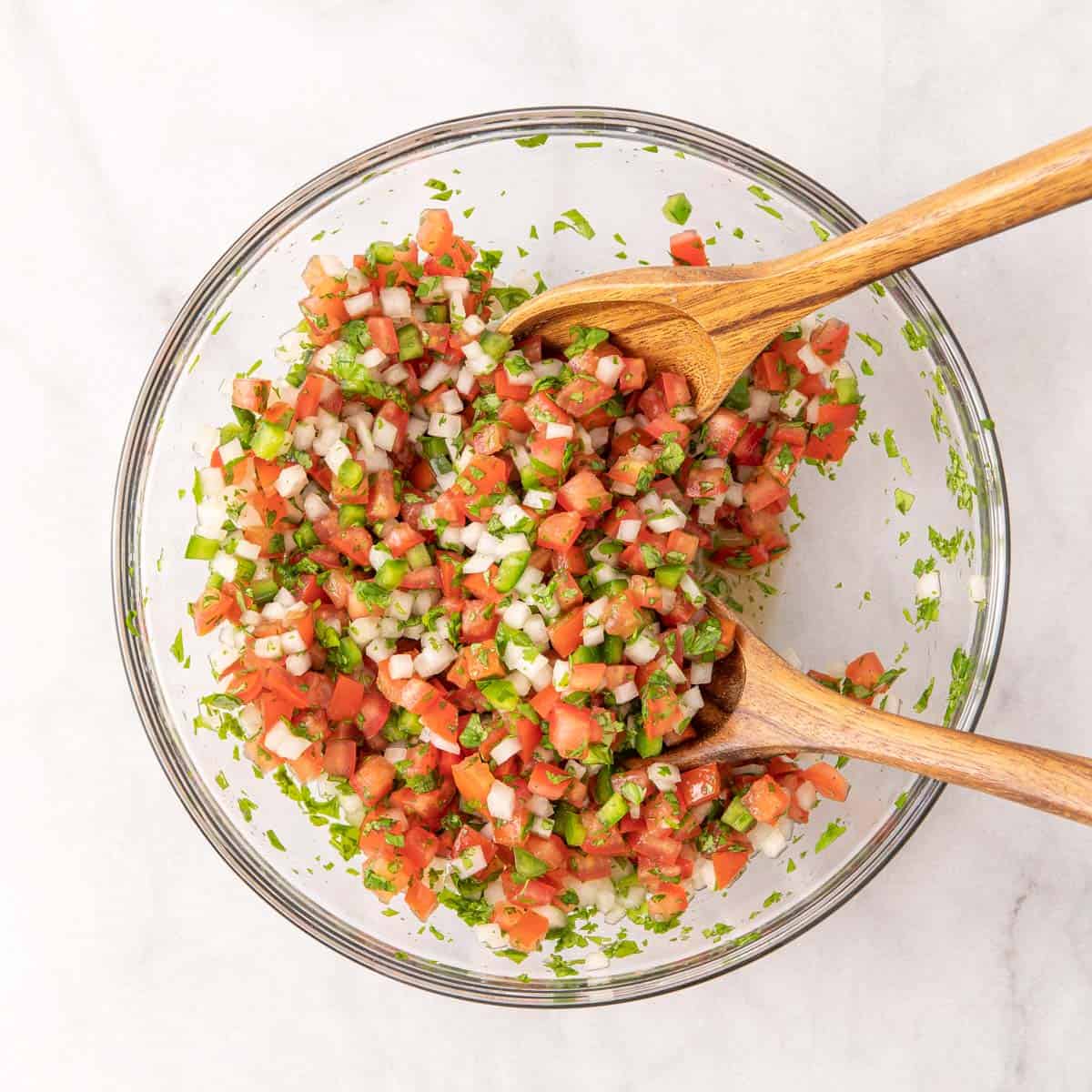 Pico de Gallo in a mixing bowl with a set of wooden salad servers in the bowl.