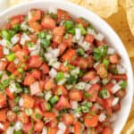 Overhead view of pico de gallo in a bowl surrounded by tortilla chips. Overlay text at top of image.