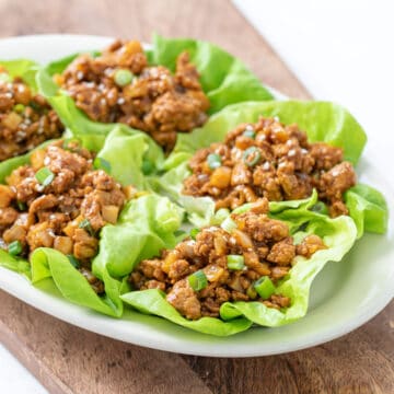 Five Asian chicken lettuce wraps on an oval white serving plate.