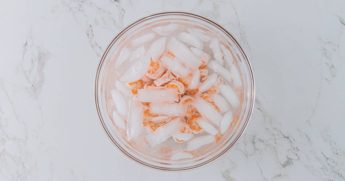 Boiled shrimp that are in a bowl of ice water.