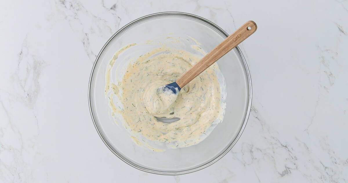 Overhead view of a bowl of mayonnaise-based dressing with a spoon for shrimp salad.