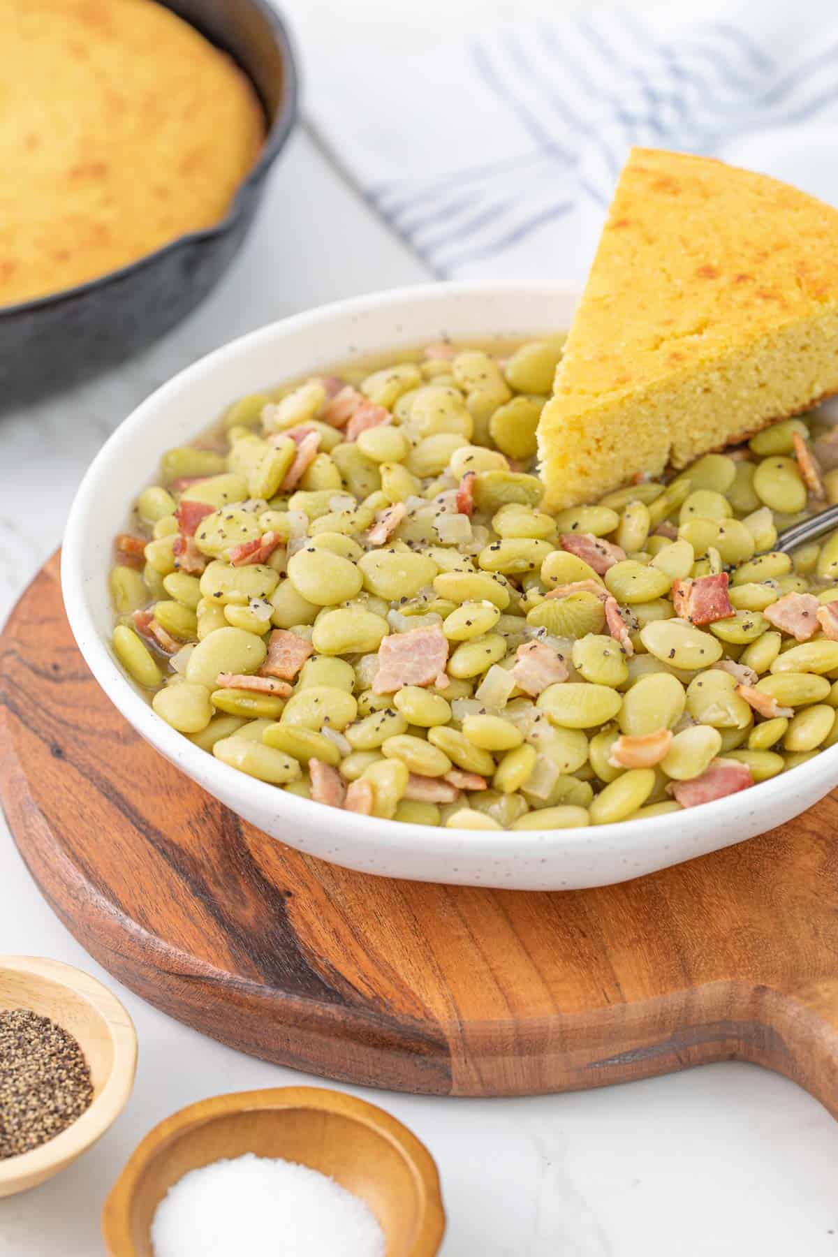 A bowl of butter beans with a slice of cornbread on a wooden trivet.