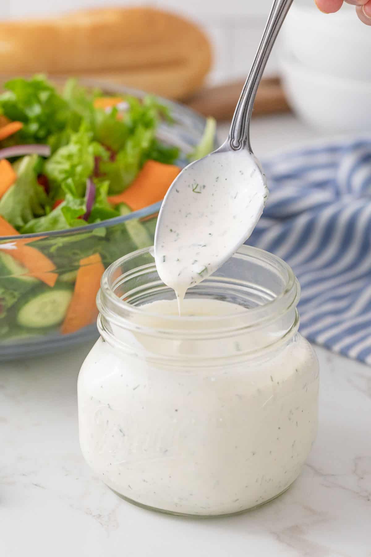 A spoon is being removed from a jar of buttermilk ranch dressing.