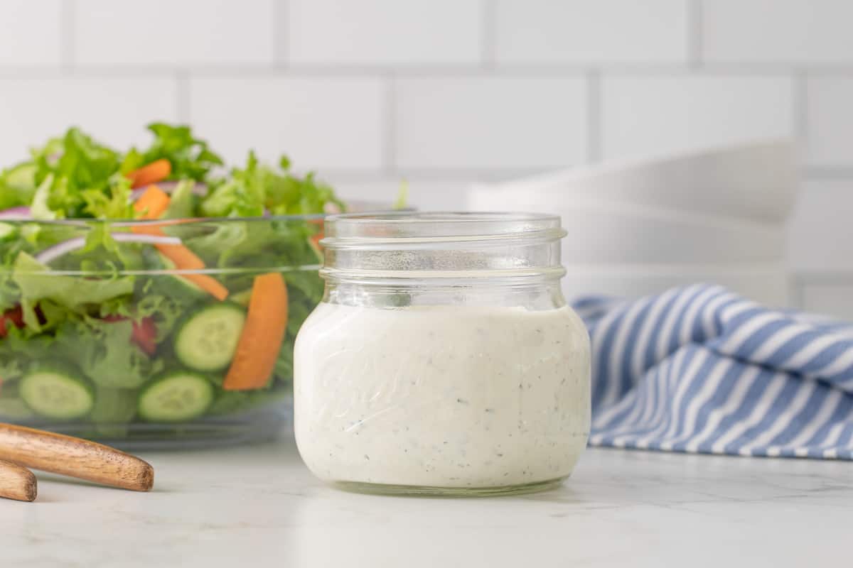 Front view of a jar of buttermilk ranch dressing. A garden salad is in the background.
