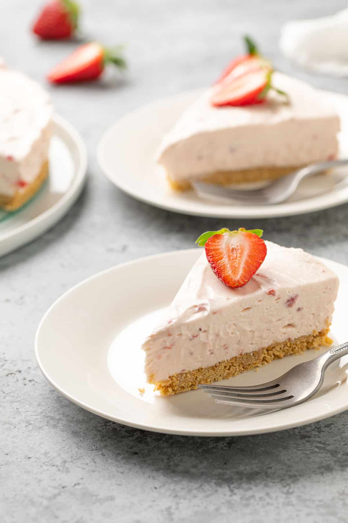 A slice of no bake strawberry cheesecake on a white dessert plate with a fork.