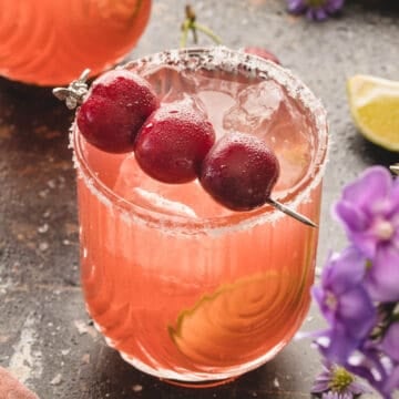 A close-up view of a cherry margarita garnished with fresh cherries in a salt-rimmed glass.