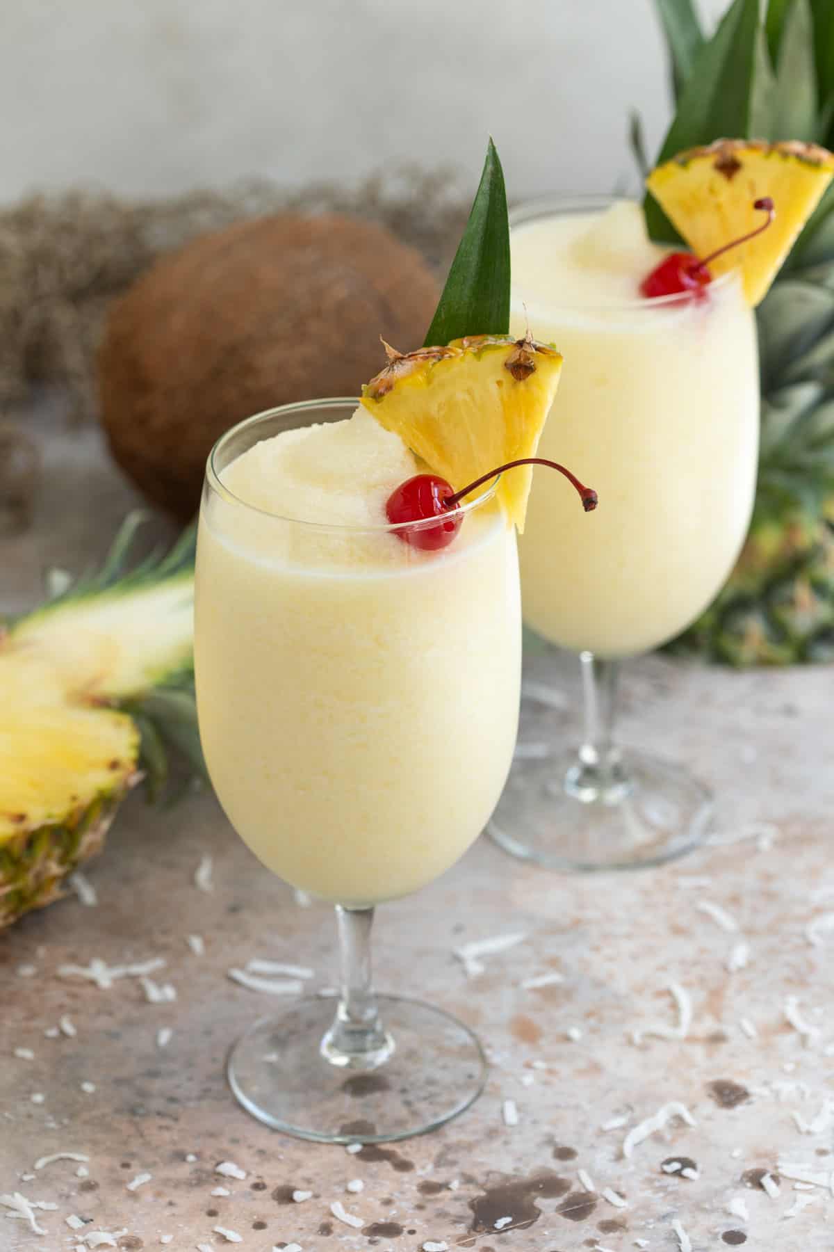 Two frozen pina coladas garnished with a pineapple wedge and a maraschino cherry.