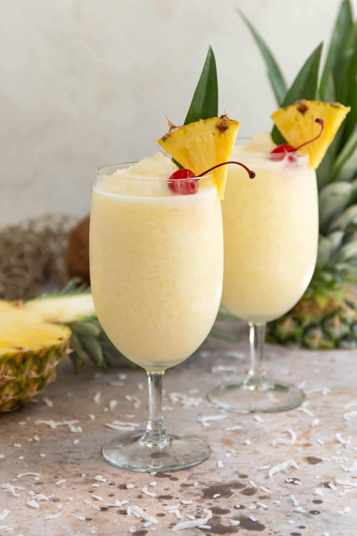 Front view of two frozen pina coladas garnished with a pineapple wedge and a maraschino cherry.