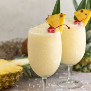 Front view of two frozen pina coladas garnished with a cherry and pineapple wedge.