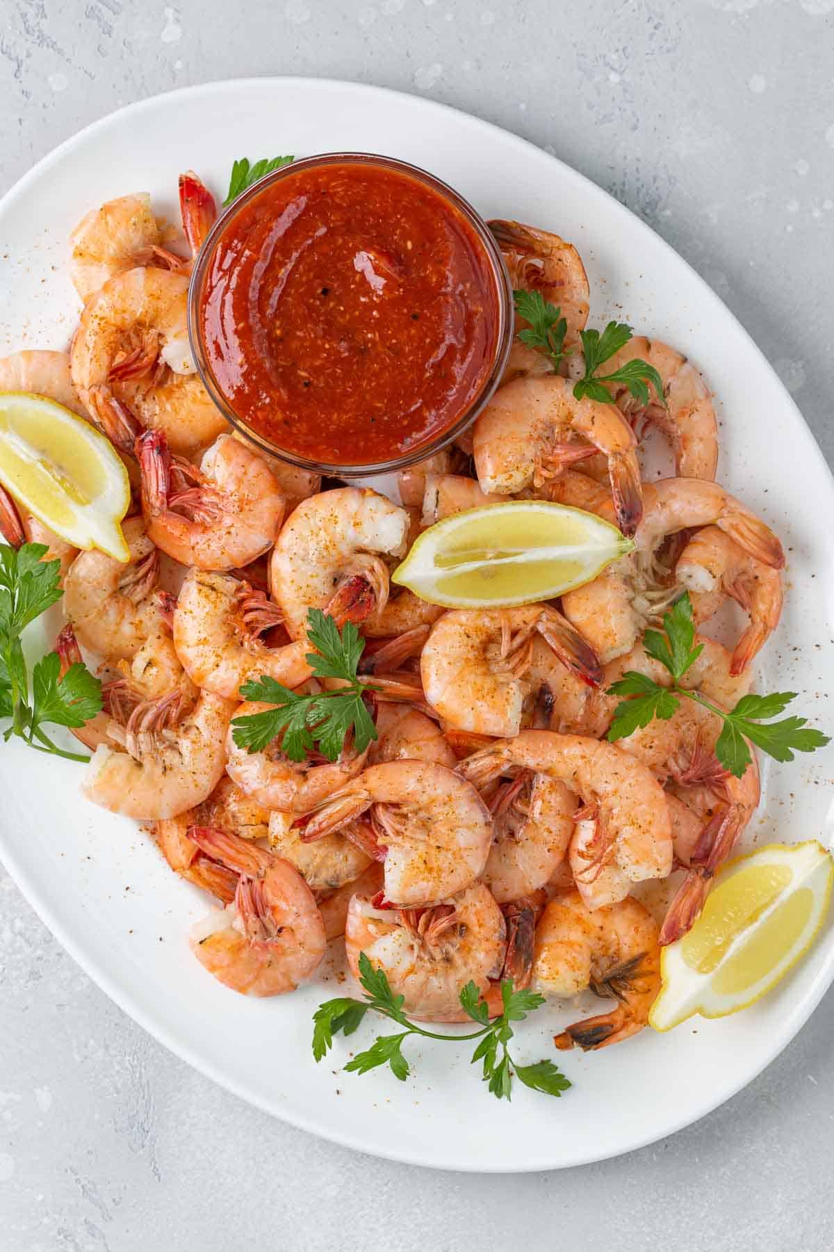 Overhead view of a bowl of cocktail sauce on an oval white platter with steamed shrimp.