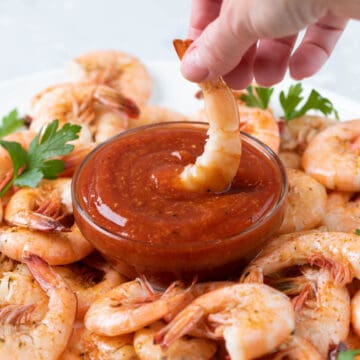 A shrimp is being dipped into a bowl of homemade cocktail sauce.