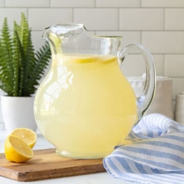 A glass pitcher of homemade lemonade by a blue and white striped kitchen towel.