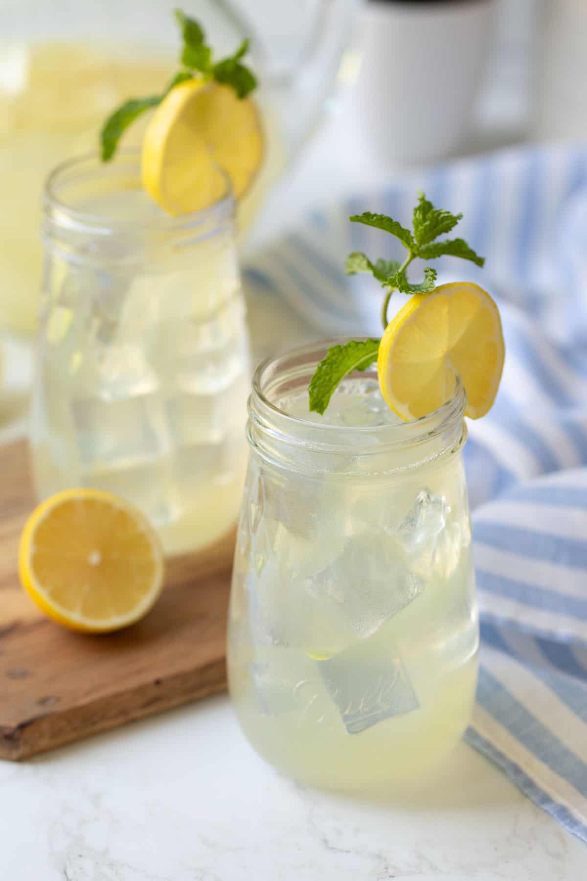 Two Mason jars of homemade lemonade garnished with a lemon wheel and mint sprig.