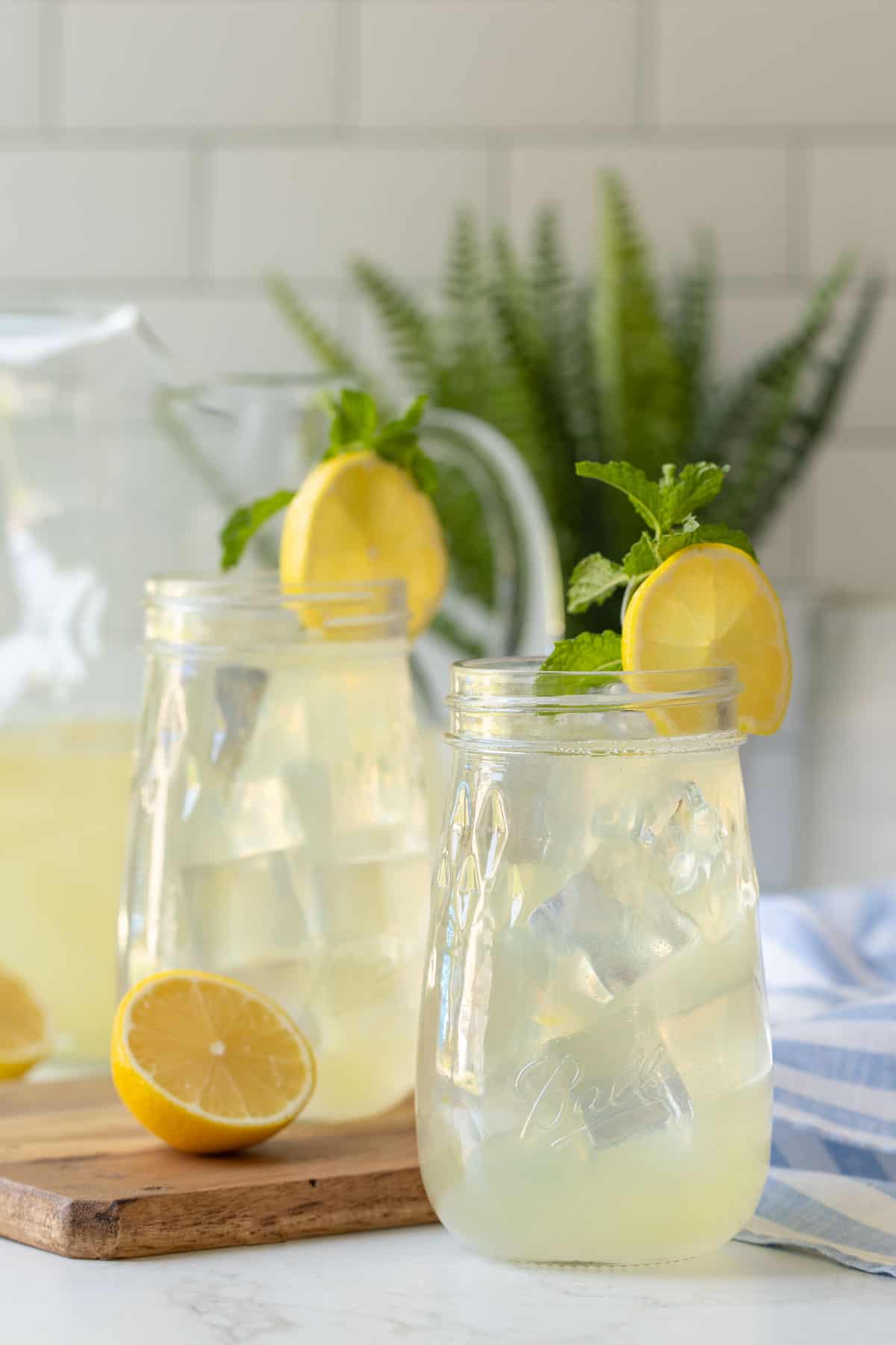 Front view of two Mason jars of lemonade garnished with lemon wheels and mint sprigs.